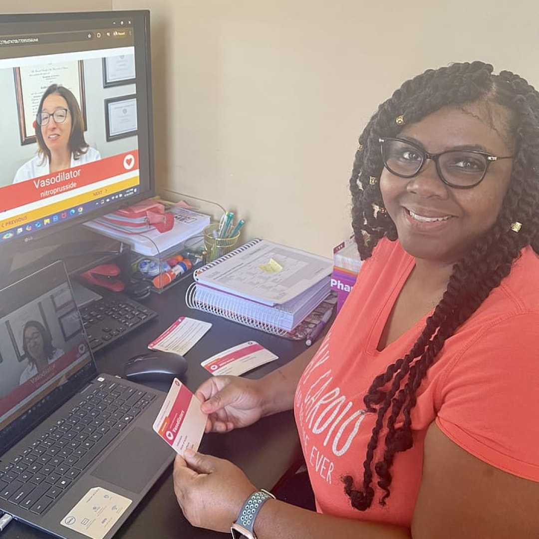 Makeka sitting at a desk with a computer watching videos and holding flashcards