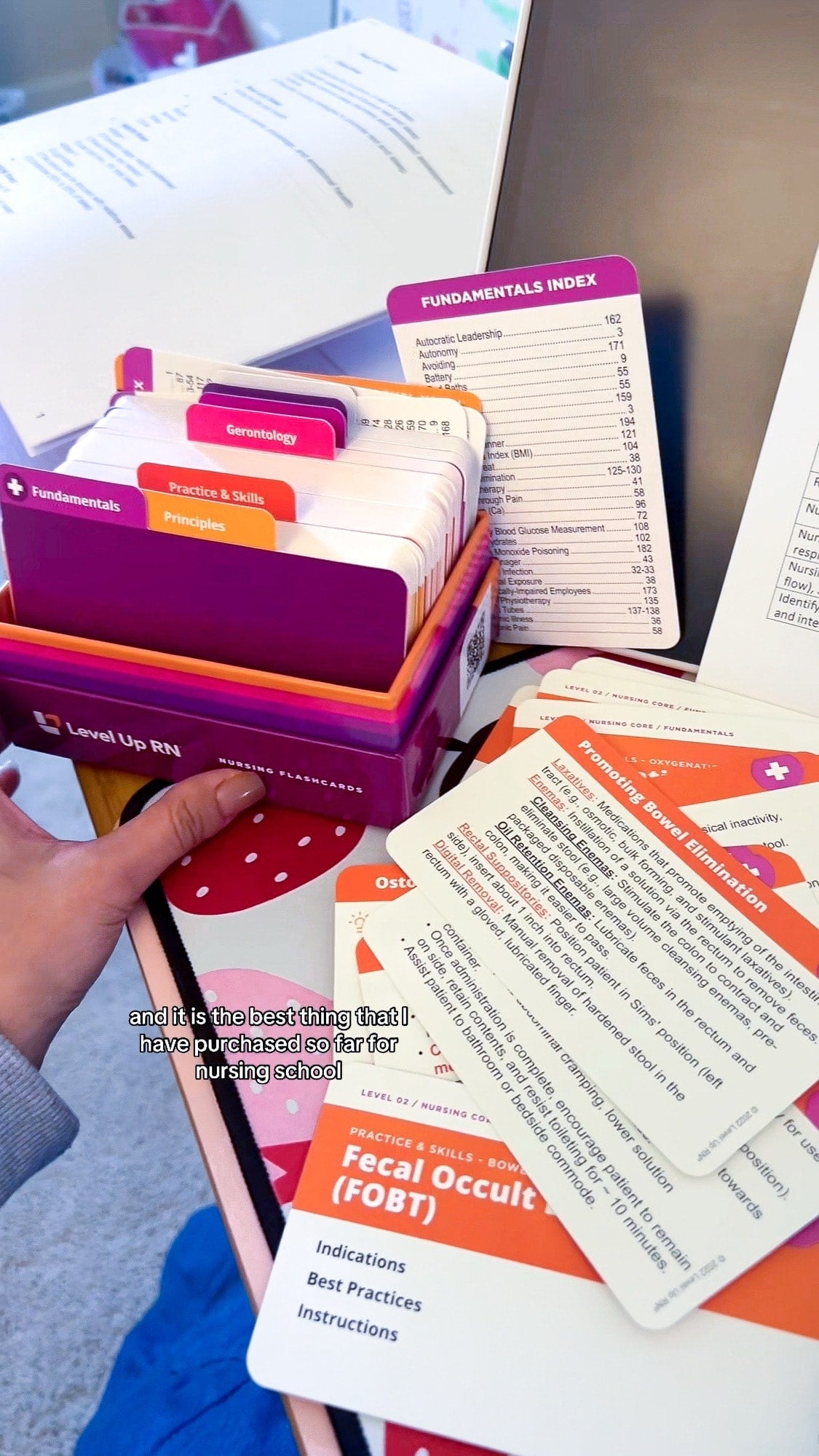 A hand covering Fundamentals flashcards with a worksheet and notebook, text on photo says "and it is the best thing that I have purchased so far for nursing school"