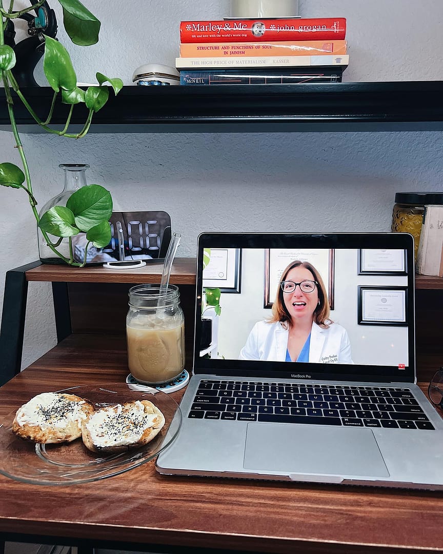 A laptop showing a Cathy Parkes RN, BSN, PHN, CWCN nursing education video next to a bagel