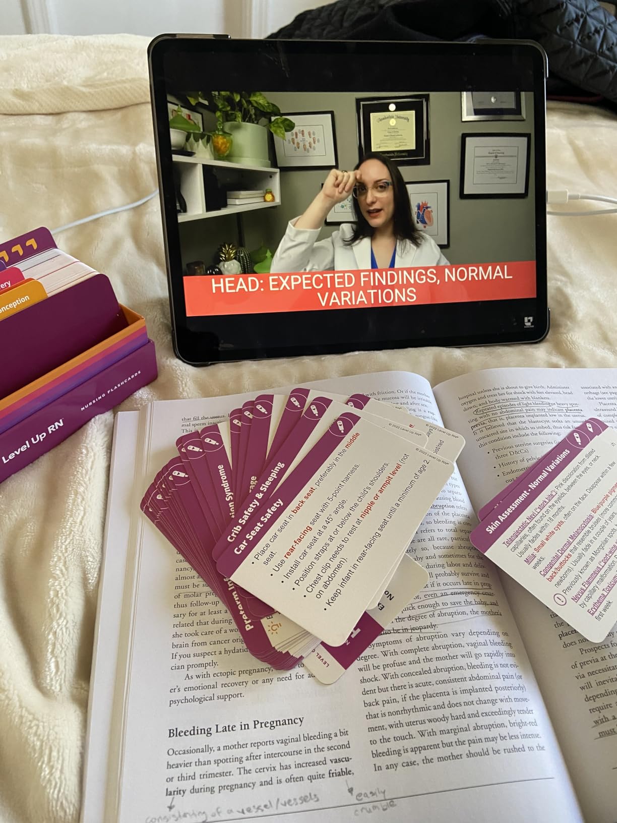 Maternity Nursing - Flashcards flashcards on a textbook and a Level Up RN nursing video with Meris Shuwarger BSN, RN, CEN, TCRN on Head, expected findings, normal variations playing on a laptop