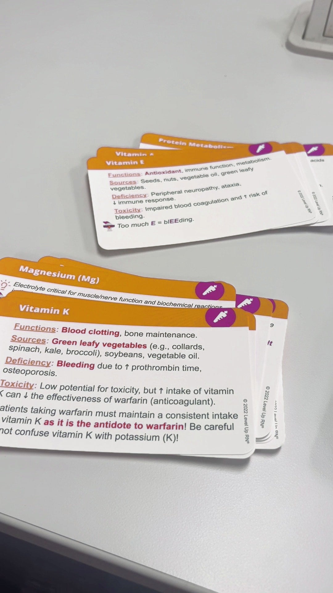 Level Up RN Nutrition Essentials - Nursing Flashcards for vitamin k, magnesium, vitamin E and more on a desk